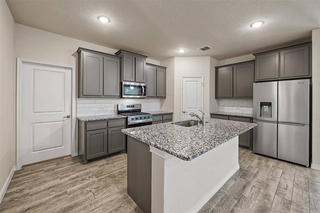 Kitchen featuring an island with a built-in sink, gray cabinetry, stainless steel appliances, porcelain tile flooring and recessed lighting