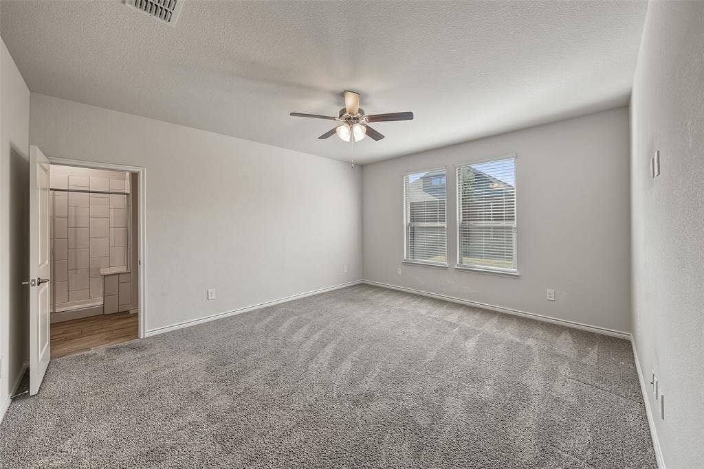 Carpeted flooring, ceiling fan with light fixture, two windows with blinds, and white interior walls