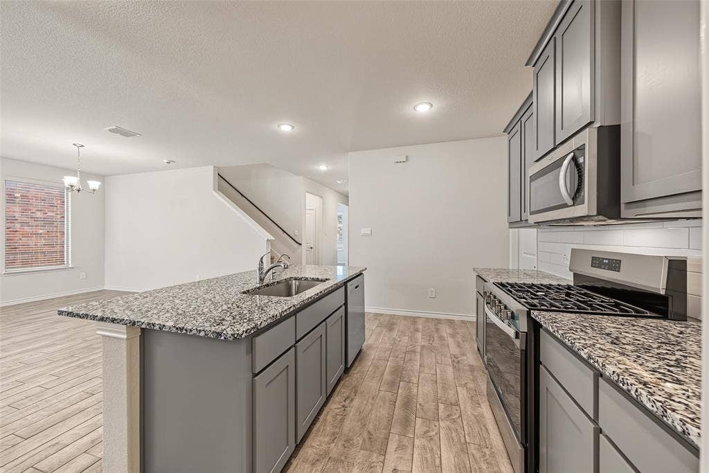 Kitchen featuring grey shaker-style cabinetry, stainless steel appliances, granite countertops, and a subway tile backsplash