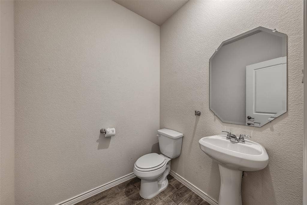 Downstairs 1/2 bath with pedestal sink w/ chrome faucet, octagonal wall mirror, and porcelain tile flooring
