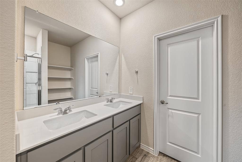 Dual vanity with undermount sinks, chrome fixtures, a large frameless mirror, and wood-finish flooring