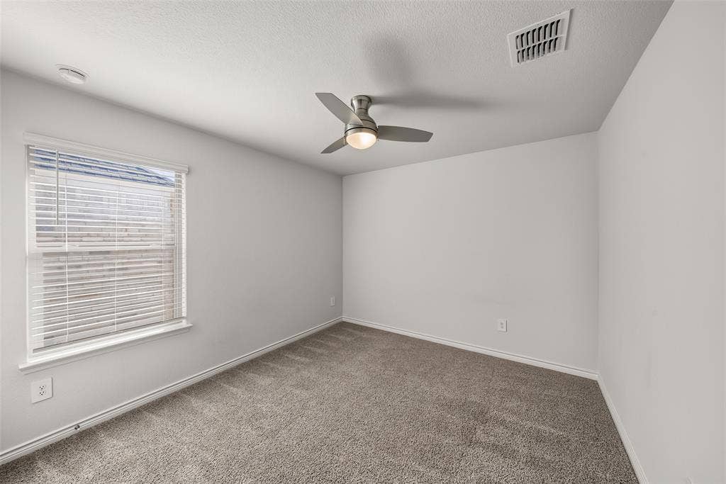Neutral wall color, carpeted flooring, window with blinds, and a ceiling fan with integrated lighting