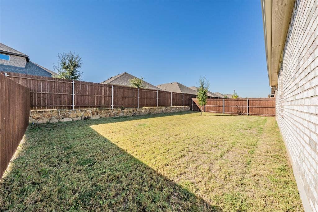 Expansive backyard featuring a natural wood privacy fence, gates on both sides of the home, stone retaining wall, and a brick exterior