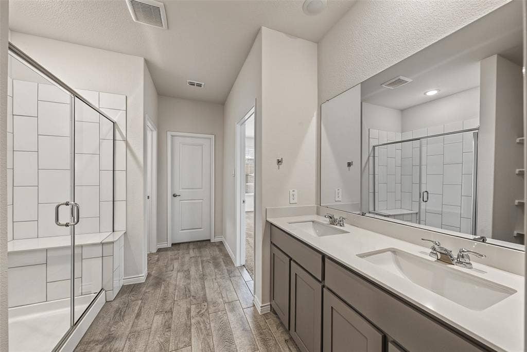 Dual vanity with integrated sinks, porcelain tile flooring, glass-enclosed shower with tiled walls and built-in bench, and a large wall-mounted mirror
