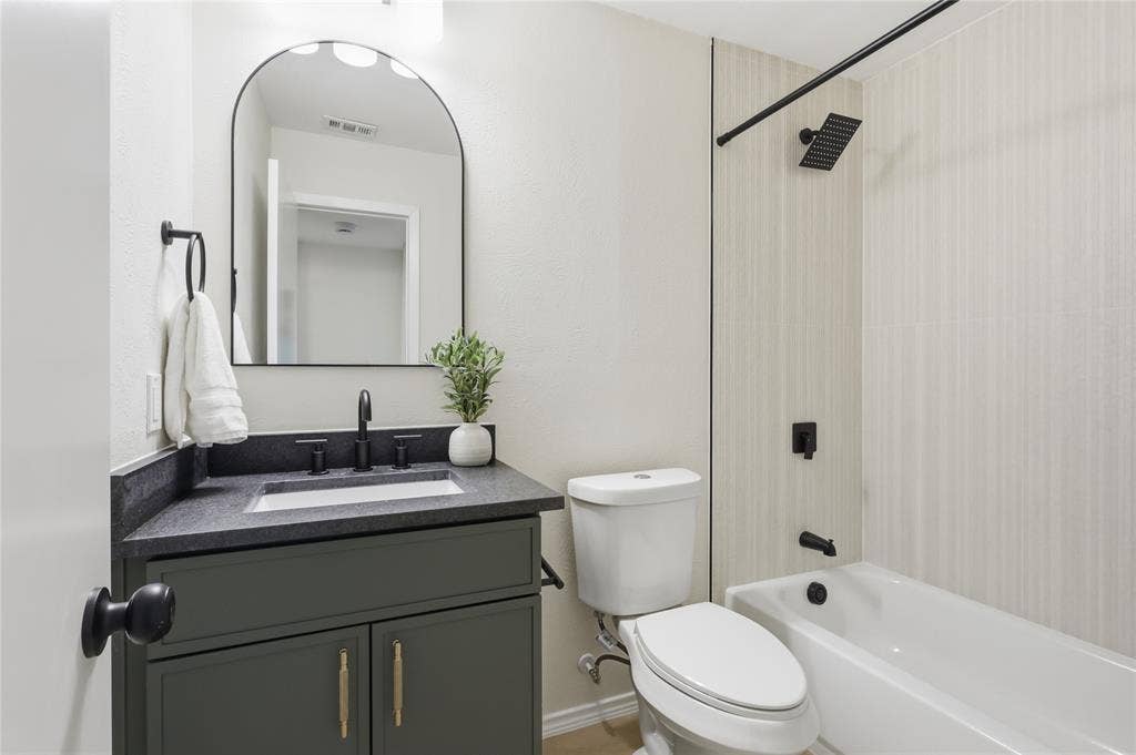 1521 Glenwick Drive, Plano, TX 75075 Dark cabinetry featuring a solid surface countertop, rectangular under-mount sink, arched mirror, and matte black hardware including a square shower head and faucet