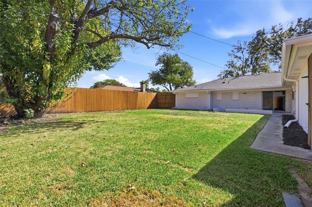 1521 Glenwick Drive, Plano, TX 75075 Backyard featuring a grass lawn, wood privacy fencing, mature trees, concrete pathway, and light-colored brick exterior