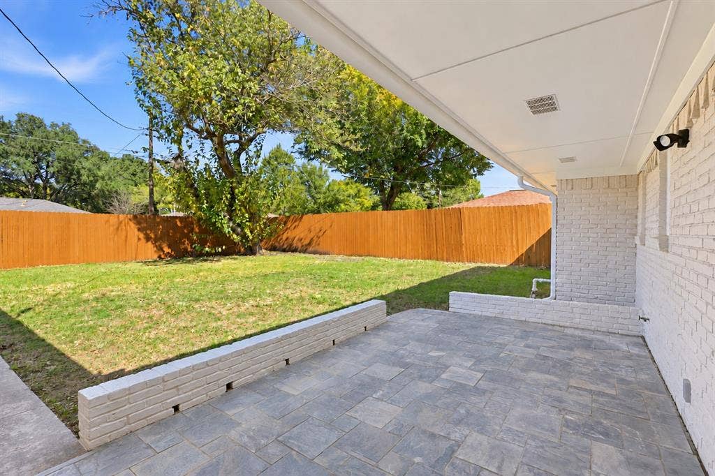 1521 Glenwick Drive, Plano, TX 75075 Covered patio featuring stone-tiled flooring, a built-in brick retaining wall, a manicured lawn, and perimeter wood privacy fencing