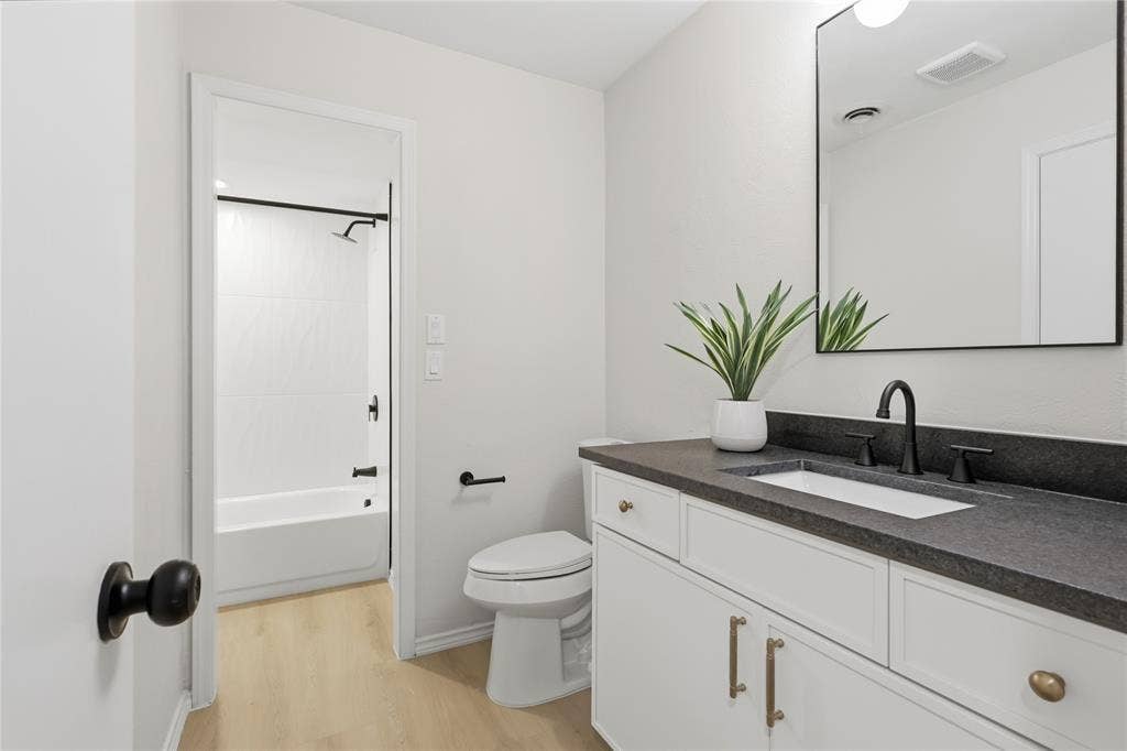 1521 Glenwick Drive, Plano, TX 75075 Bathroom featuring a white vanity cabinet with stone-finish countertop, under-mount rectangular sink, matte black fixtures, and a frameless wall-mounted mirror