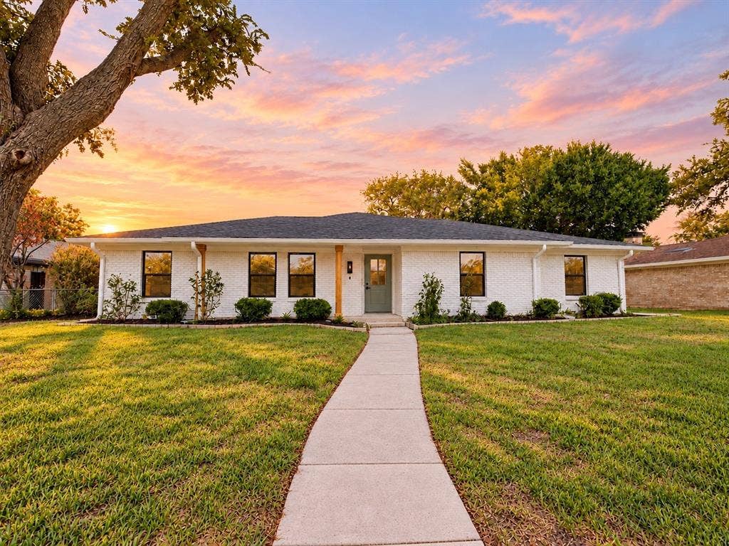 1521 Glenwick Drive, Plano, TX 75075 White painted brick exterior featuring a low-pitch roof, dark-framed windows, a centered entry door, and a concrete walkway