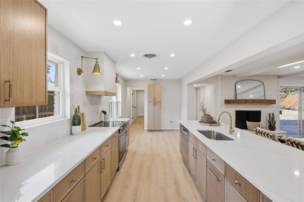1521 Glenwick Drive, Plano, TX 75075 Kitchen featuring light wood-finish cabinetry, quartz countertops, a central island with an undermount sink, recessed lighting, and a painted brick fireplace with a wood mantel