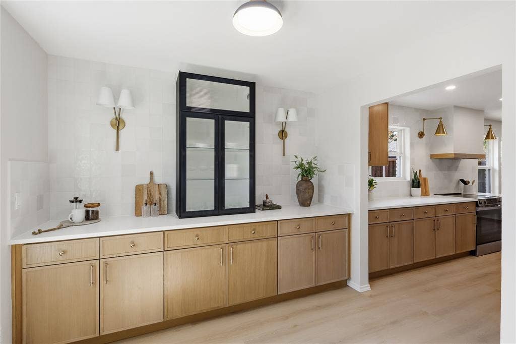 1521 Glenwick Drive, Plano, TX 75075 Kitchen featuring custom light-wood cabinetry, white solid-surface countertops, integrated glass-front display cabinetry, brass-toned wall sconces, and wood-finish flooring