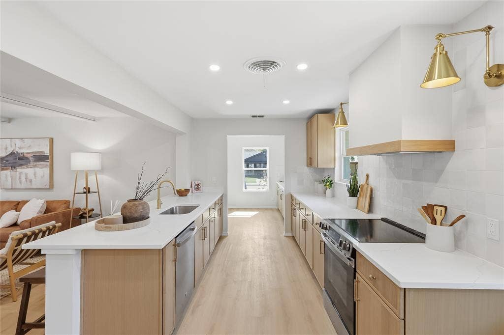 1521 Glenwick Drive, Plano, TX 75075 Kitchen featuring light wood-finish cabinetry, white solid-surface countertops, subway-style tile backsplash, stainless steel appliances, and brass-finish wall-mounted lighting
