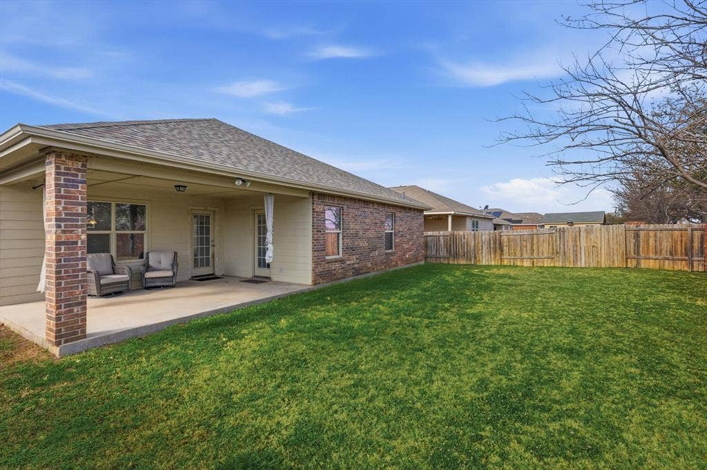 Expansive backyard featuring a lush lawn, privacy fencing, and a covered concrete patio