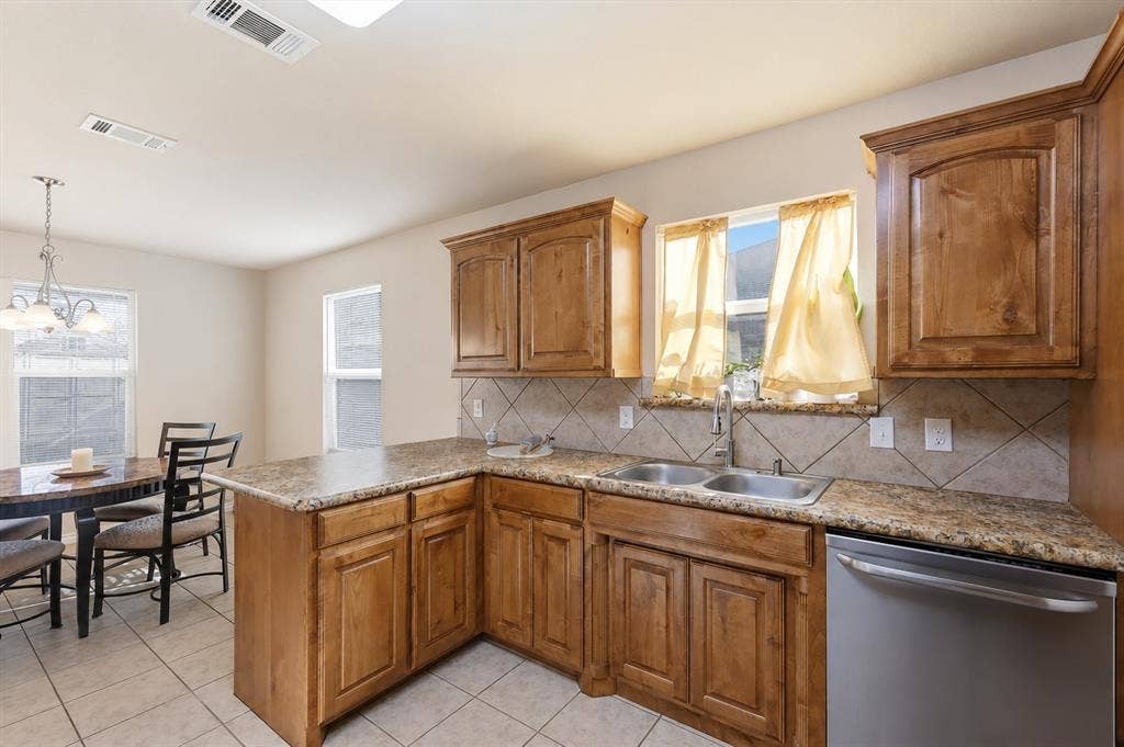 Kitchen featuring wood cabinetry, stone-finish countertops, a tile backsplash, and a stainless steel dishwasher