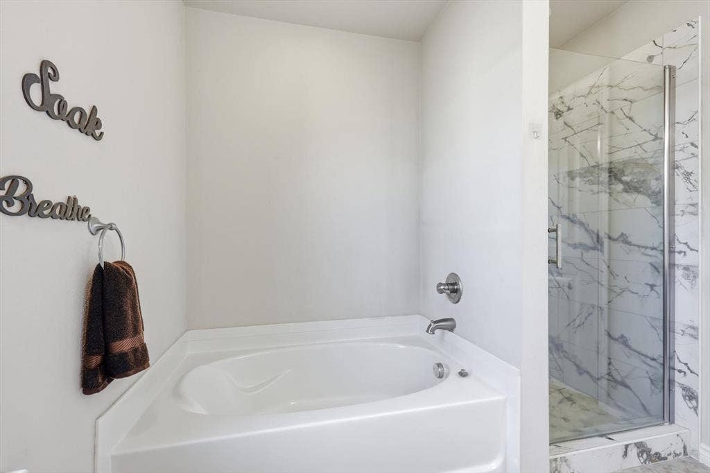 Corner soaking tub with polished chrome fixtures and a glass-enclosed shower featuring marble-look tile
