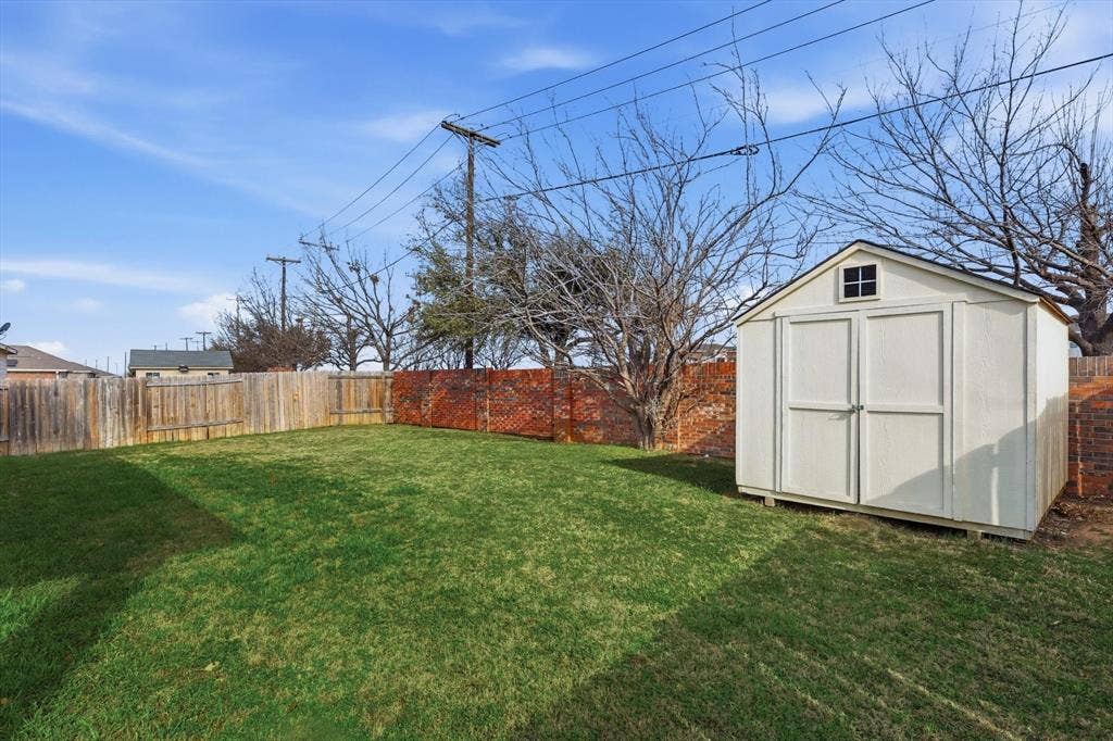 Expansive backyard featuring a manicured lawn, wood privacy fencing, and a brick accent wall