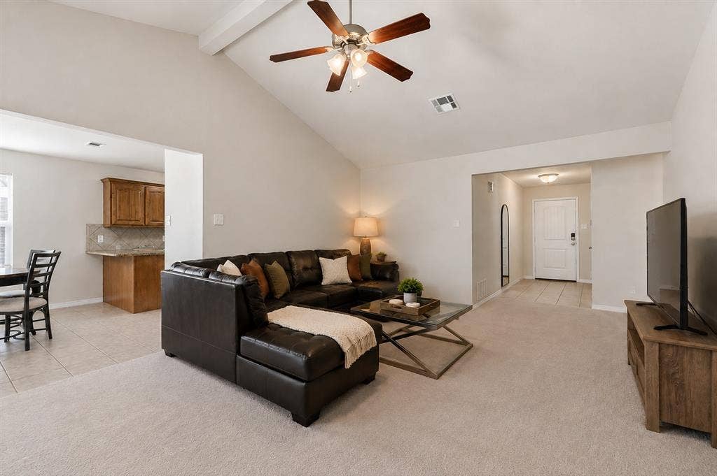 Vaulted ceiling with an exposed beam, ceiling fan with light, recessed lighting, and a kitchen with wood cabinetry