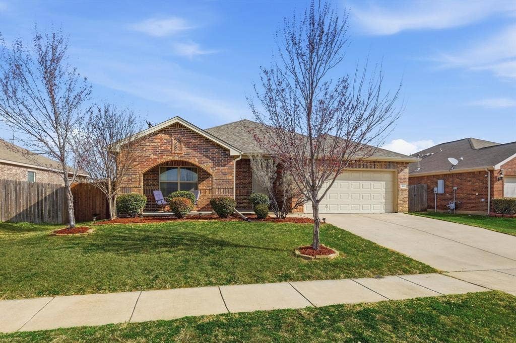 Brick exterior with an arched entryway, attached garage, concrete driveway, and a fenced side yard