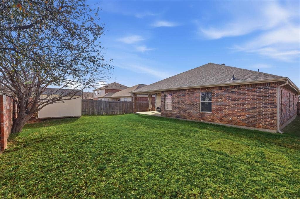 Expansive backyard featuring a manicured lawn, brick exterior, covered patio, and wood privacy fencing