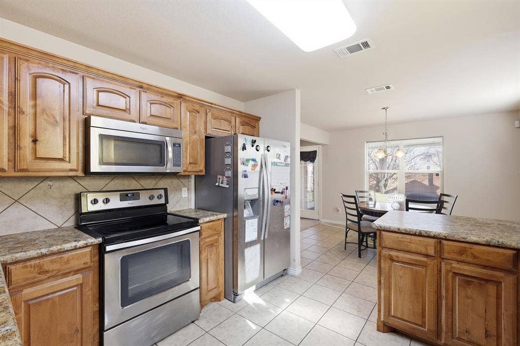 Kitchen featuring wood cabinetry, stainless steel appliances, tile flooring, and stone-finish countertops