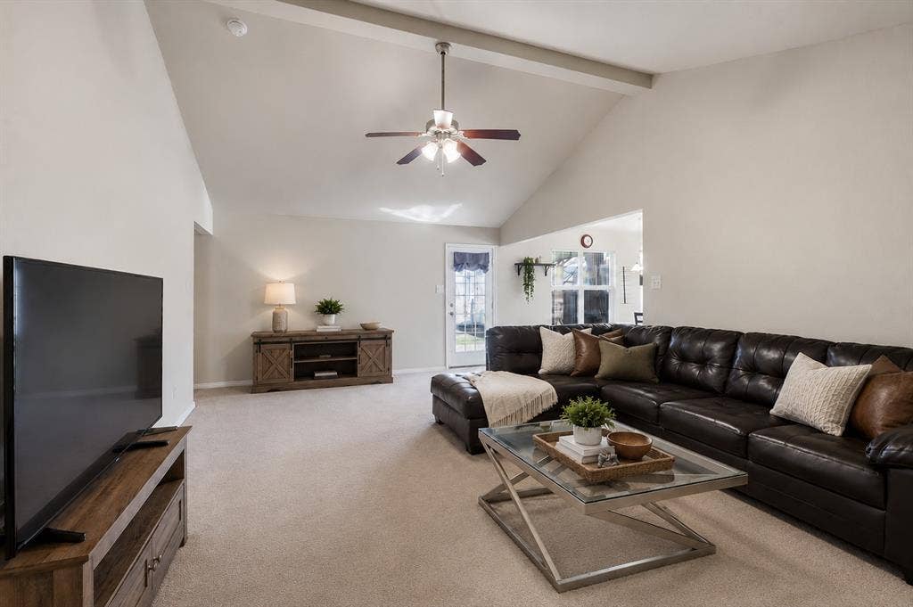 Vaulted ceiling with exposed beam, ceiling fan, and light-toned carpet flooring