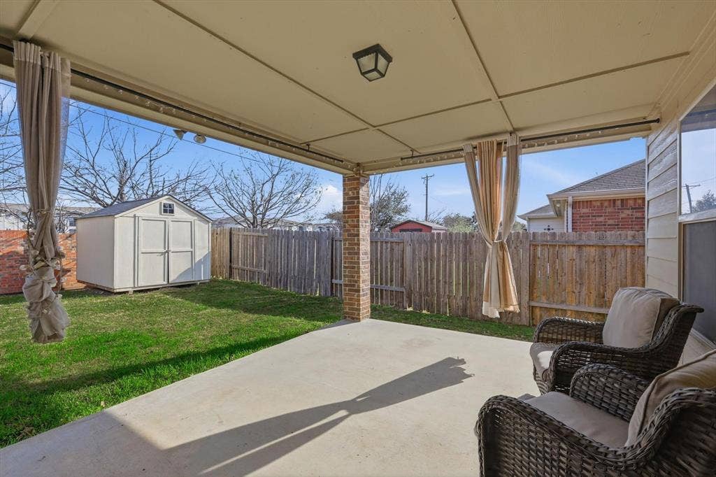Covered patio with concrete flooring, wood privacy fencing, and a detached storage shed