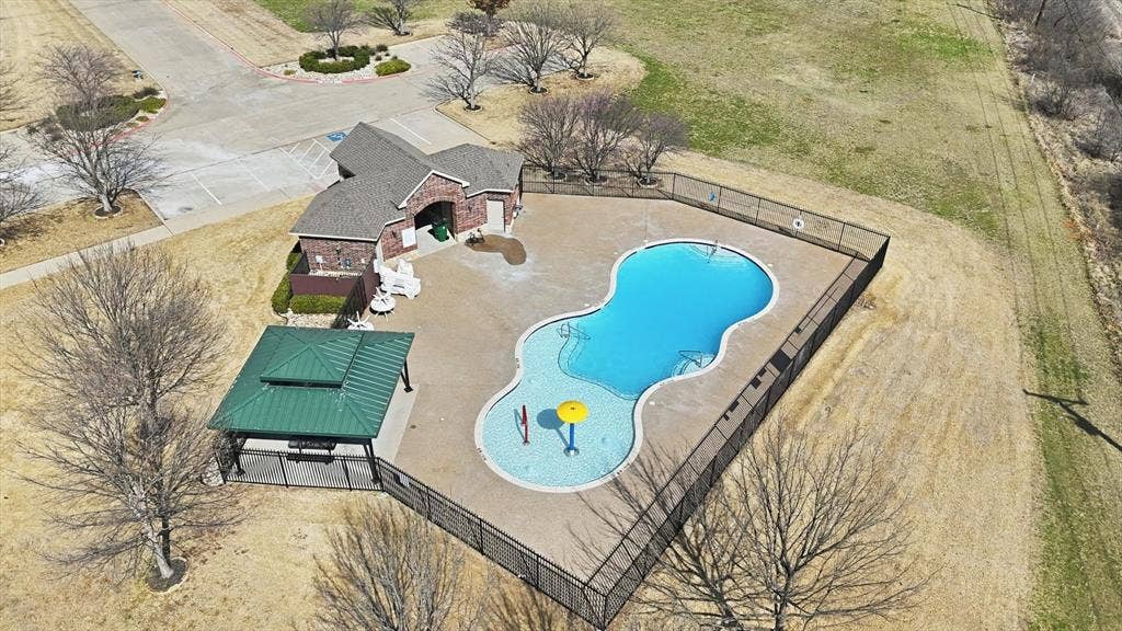 Freeform swimming pool with surrounding fence, adjacent building with brick exterior, and covered gazebo