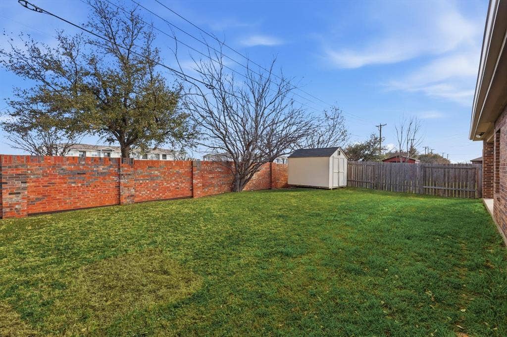 Expansive grass lawn with a brick perimeter wall, wood fence, and a detached storage shed