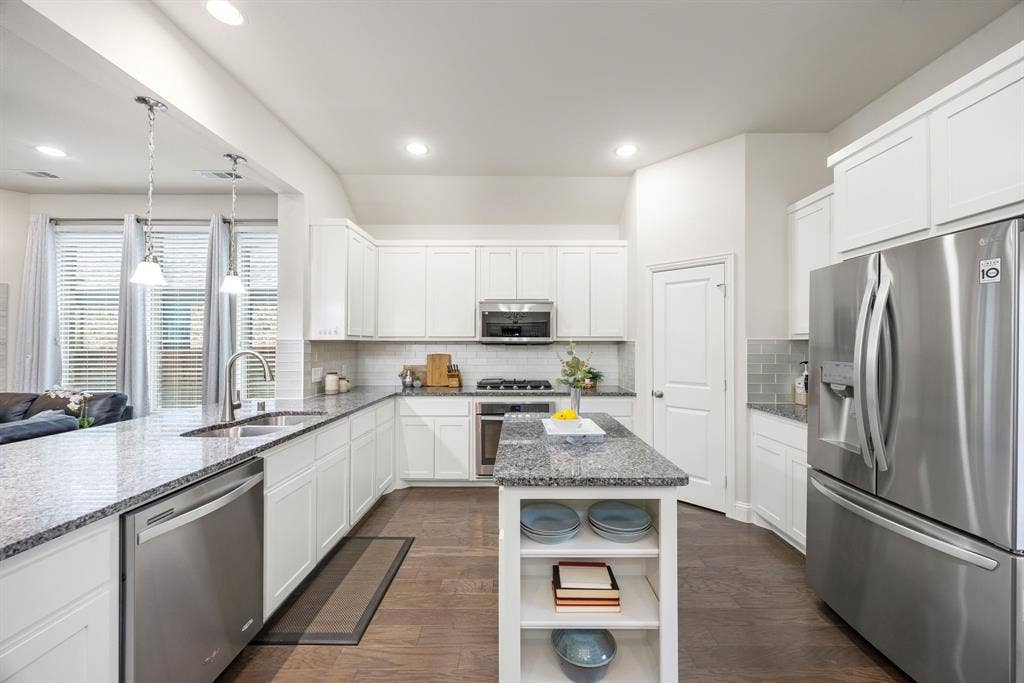 908 Spring Falls Drive, McKinney, TX 75071 Modern kitchen featuring white cabinetry, stainless steel appliances, a center island with built-in shelving, durable wood-finish flooring, and recessed lighting