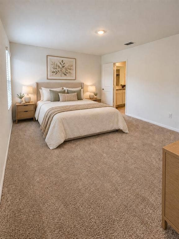 *Virtually Staged* Spacious primary bedroom featuring neutral carpeting, recessed lighting, natural light, and direct access to the en-suite bathroom and walk-in closet.