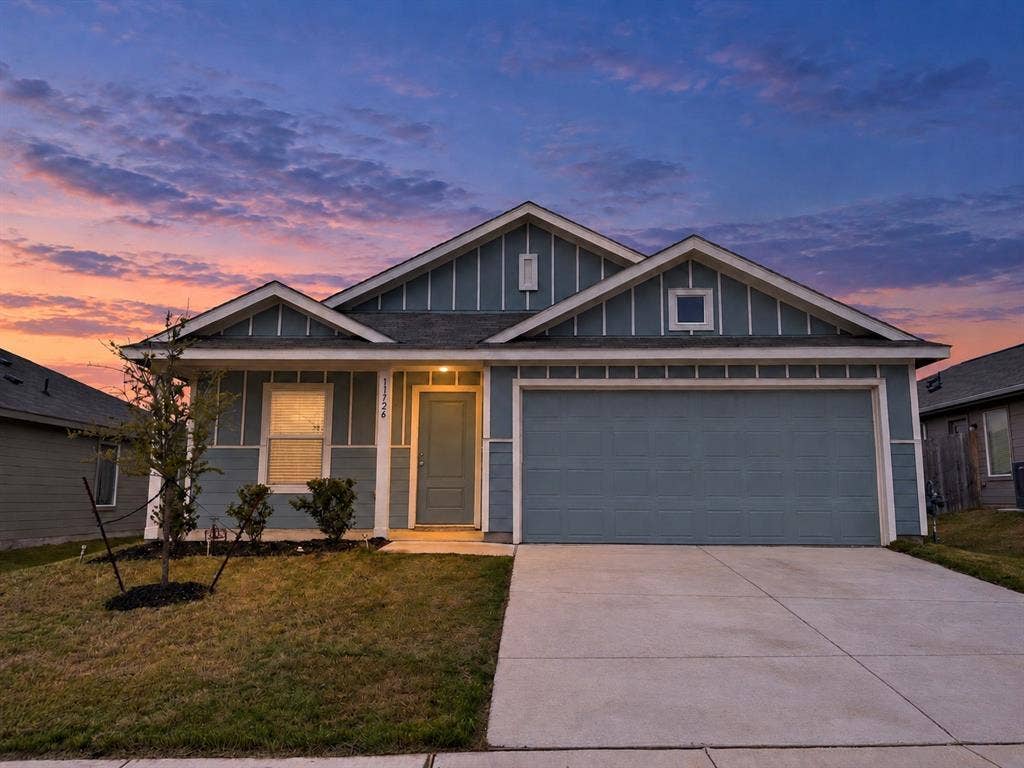 *Digitally Enhanced* Front exterior at twilight showcasing the home’s inviting covered entry, distinctive blue-and-white exterior, and attached two-car garage.