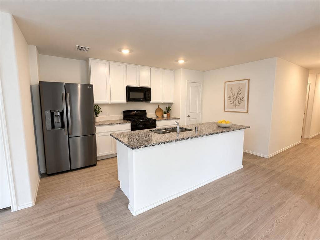 *Digitally Enhanced* Open-concept kitchen featuring granite countertops, a spacious center island, white cabinetry, black appliances, recessed lighting, and luxury vinyl plank flooring. Refrigerator included.