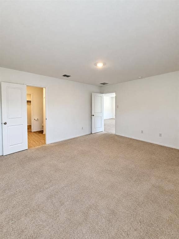 Spacious primary bedroom featuring neutral carpeting, recessed lighting, natural light, and direct access to the en-suite bathroom and walk-in closet.