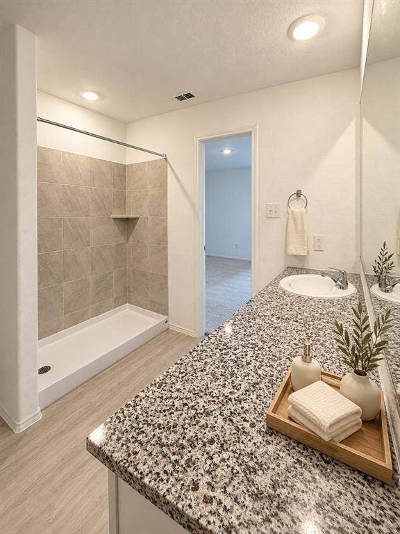 En-suite primary bath featuring a granite countertop vanity, tiled tub and shower surround, recessed lighting, and luxury vinyl plank flooring.