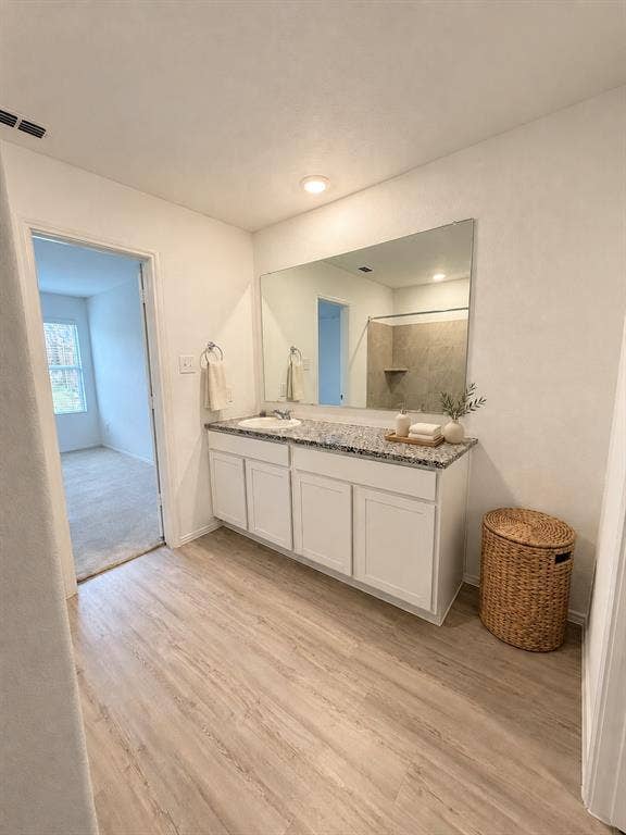 *Virtually Staged* En-suite primary bath featuring a granite countertop vanity, tiled tub and shower surround, recessed lighting, and luxury vinyl plank flooring.