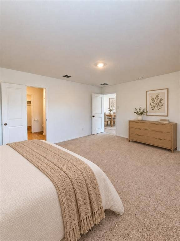 *Virtually Staged* Spacious primary bedroom featuring neutral carpeting, recessed lighting, natural light, and direct access to the en-suite bathroom and walk-in closet.