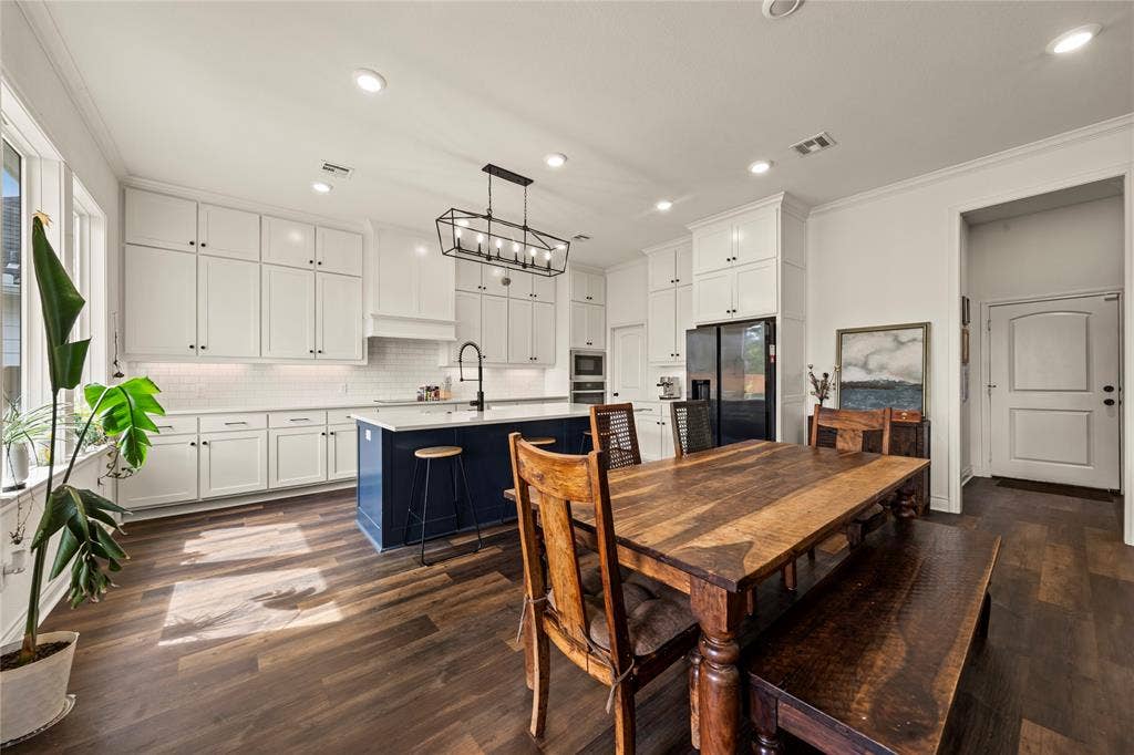 Spacious kitchen featuring white shaker cabinetry, an expansive island with a contrasting blue base, wood-finish flooring, a white subway tile backsplash, and recessed lighting