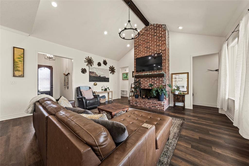 Vaulted ceiling with exposed wood beam, brick fireplace with wood mantel, recessed lighting, and wood-finish flooring
