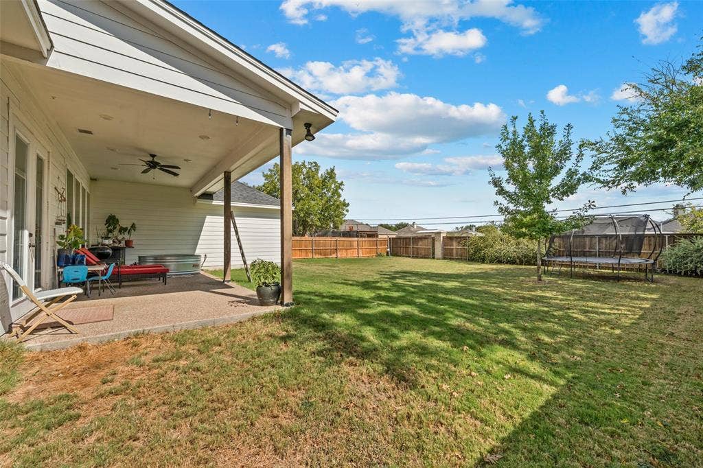 Expansive backyard featuring a covered patio, ceiling fan, and mature trees