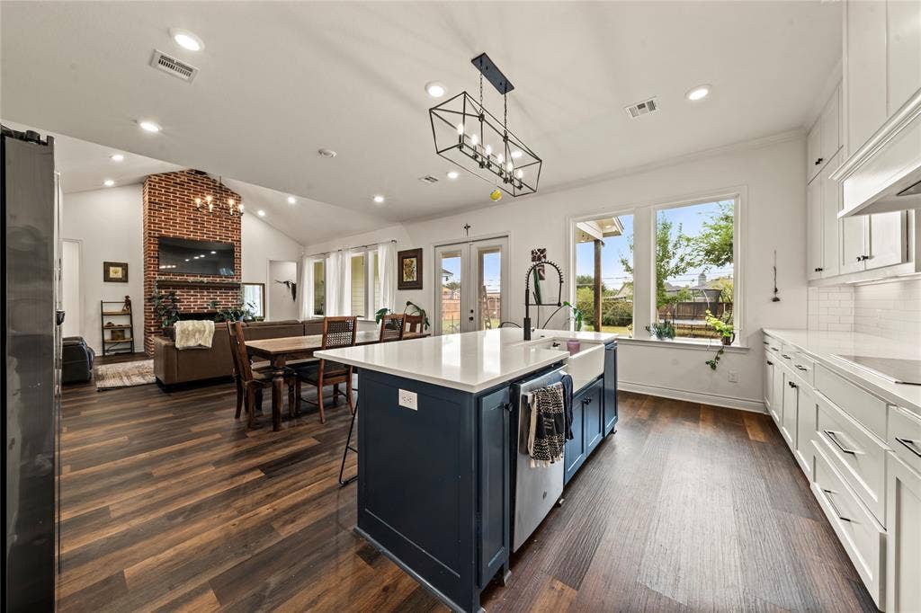 Spacious kitchen featuring an island with a farmhouse sink, white cabinetry with dark hardware, and wood-finish flooring
