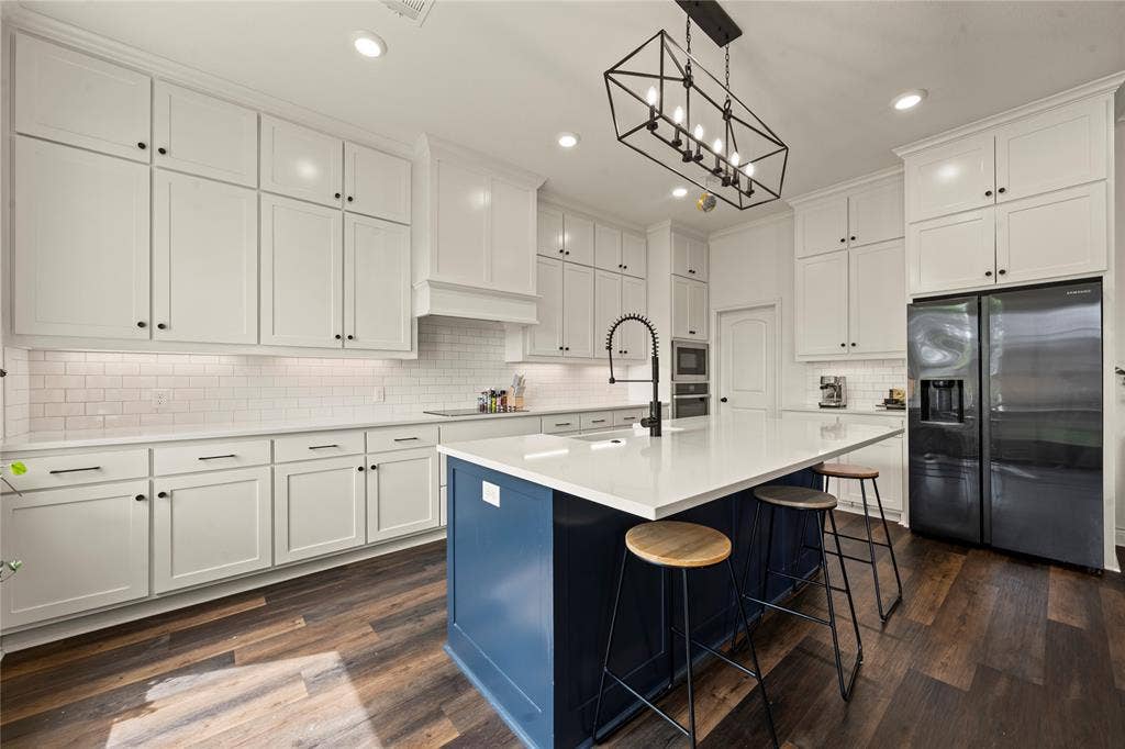 Expansive kitchen featuring a large central island with seating, white shaker cabinetry, wood-finish flooring, and a subway tile backsplash