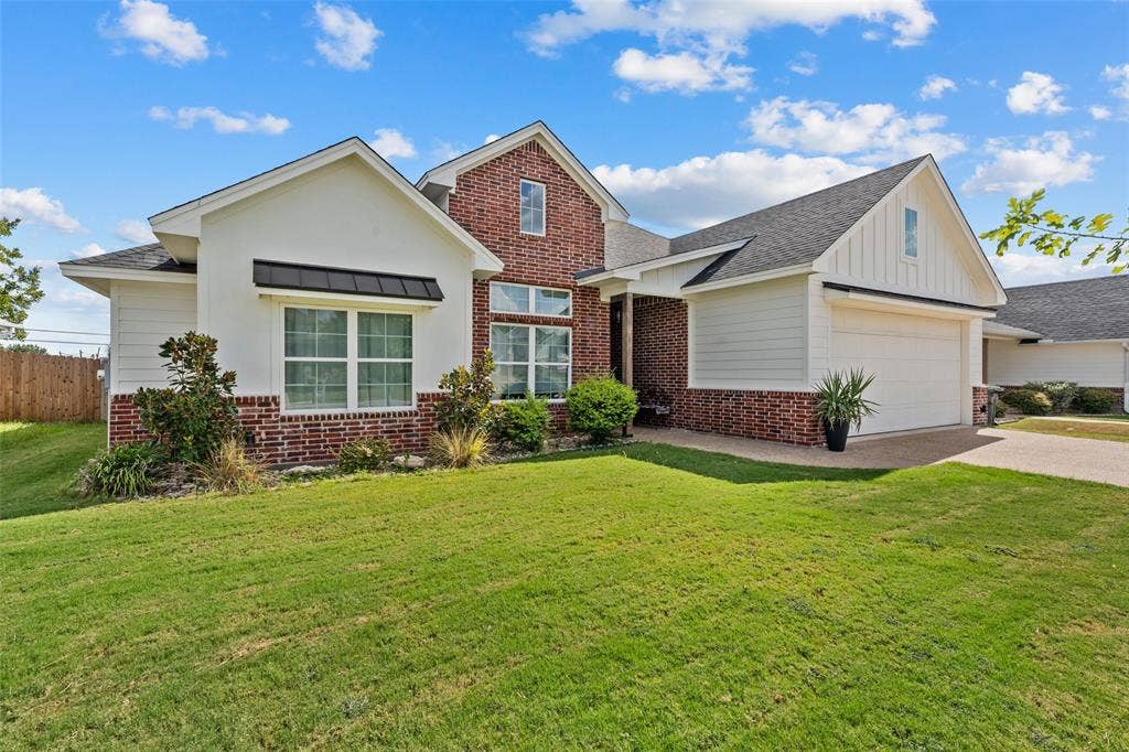 Brick and stucco exterior, arched portico entry, attached garage, dark shingle roofing, and front landscaping