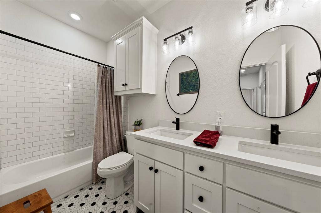 Dual vanity with undermount sinks and black fixtures, white cabinetry, and two round mirrors