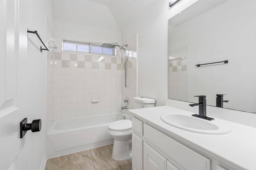 3307 Meadow Wood Drive, Richardson, TX 75082 White subway tile shower surround with a decorative accent band, tub, vanity with a white countertop, and a black matte faucet