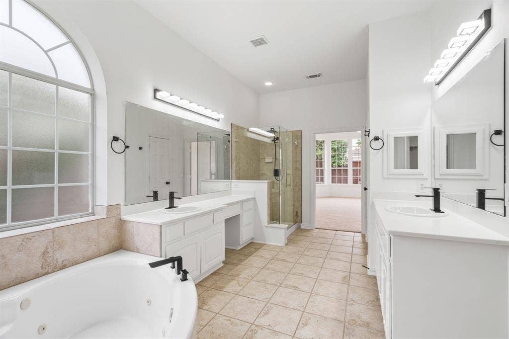 3307 Meadow Wood Drive, Richardson, TX 75082 Spacious bathroom featuring a jetted soaking tub, walk-in shower with glass enclosure, dual vanities with white cabinetry and integrated sinks, and an arched transom window