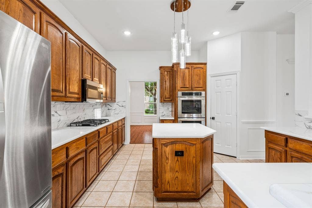 3307 Meadow Wood Drive, Richardson, TX 75082 Kitchen featuring wood cabinetry, stainless steel appliances, white countertops, tile flooring, and a decorative pendant light fixture
