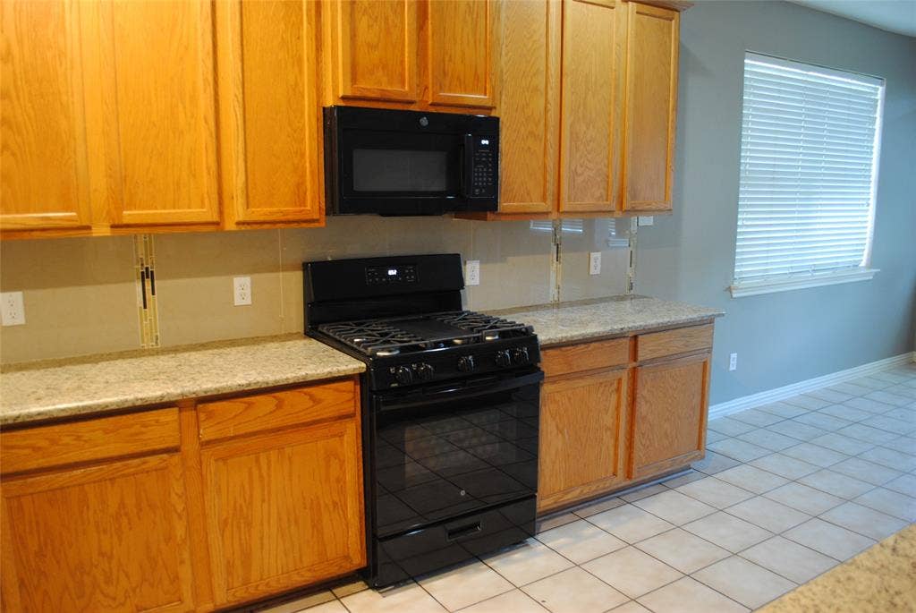 5108 Blackwood Drive, McKinney, TX 75071 Kitchen featuring light wood cabinetry, stone countertops, black gas range, built-in microwave, and tile flooring