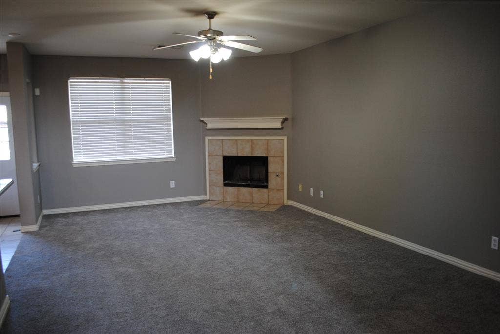 5108 Blackwood Drive, McKinney, TX 75071 Spacious living area featuring plush carpeting, a corner fireplace with tile surround and mantel, and a ceiling fan with integrated lighting