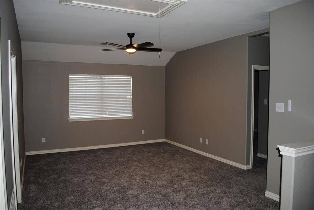 5108 Blackwood Drive, McKinney, TX 75071 Spacious media room with gray wall paint, dark carpet flooring, window with horizontal blinds, and a ceiling fan with integrated lighting