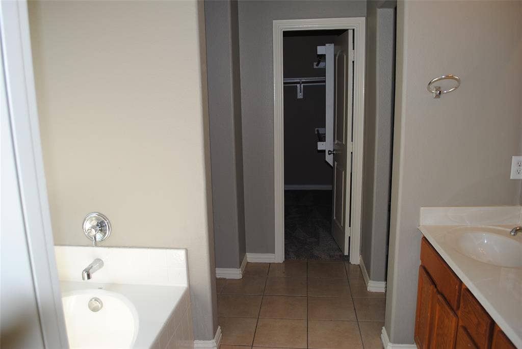 5108 Blackwood Drive, McKinney, TX 75071 Bathroom featuring a built-in bathtub with chrome fixtures, a vanity with wood-finish cabinetry, a white countertop with an integrated sink, and tile flooring